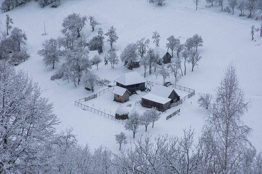 A serene aerial view of a snow-covered village in Sartăș, Romania, during winter.