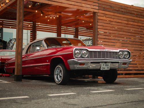 Free Classic red Chevrolet Impala displayed outdoors under wooden structure. Perfect for vintage car enthusiasts. Stock Photo