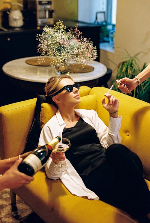 Free Woman Lying on Sofa Having her Cigarette Lit and Wine Poured Stock Photo