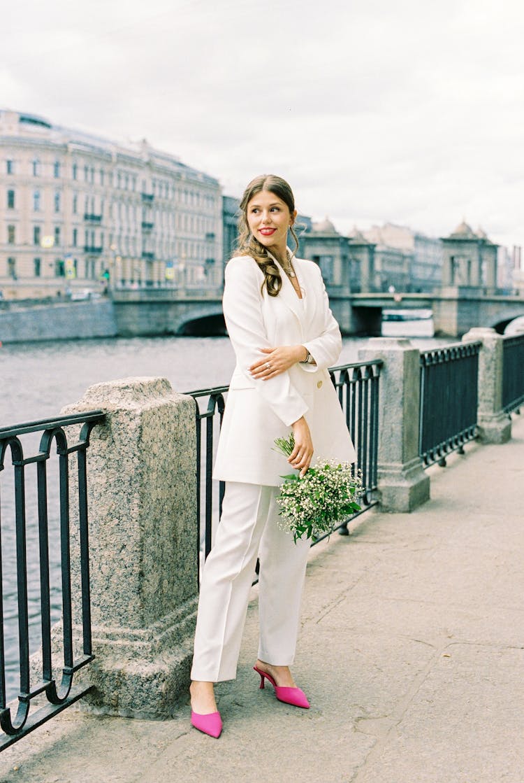 Nice Young Woman In White Suit Standing On Old Town Embankment And Smiling