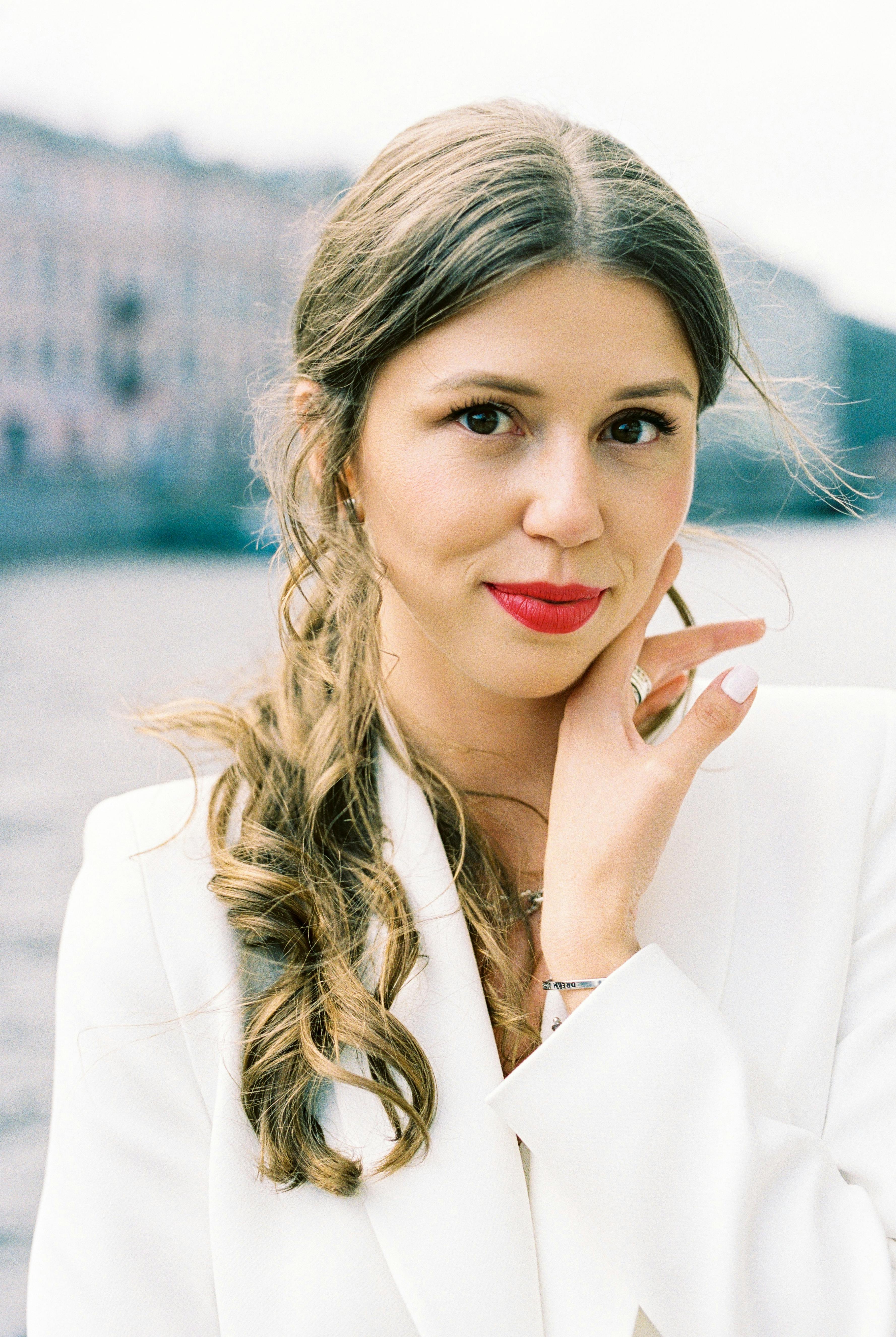 Portrait of a smiling woman in a white blazer with curly hair near a river.