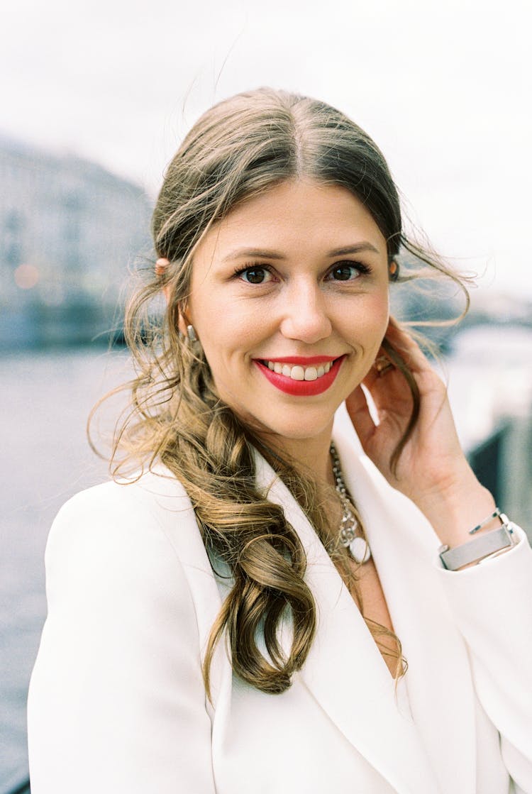 Portrait Of Young Woman In White Suit Touching Hair And Smiling