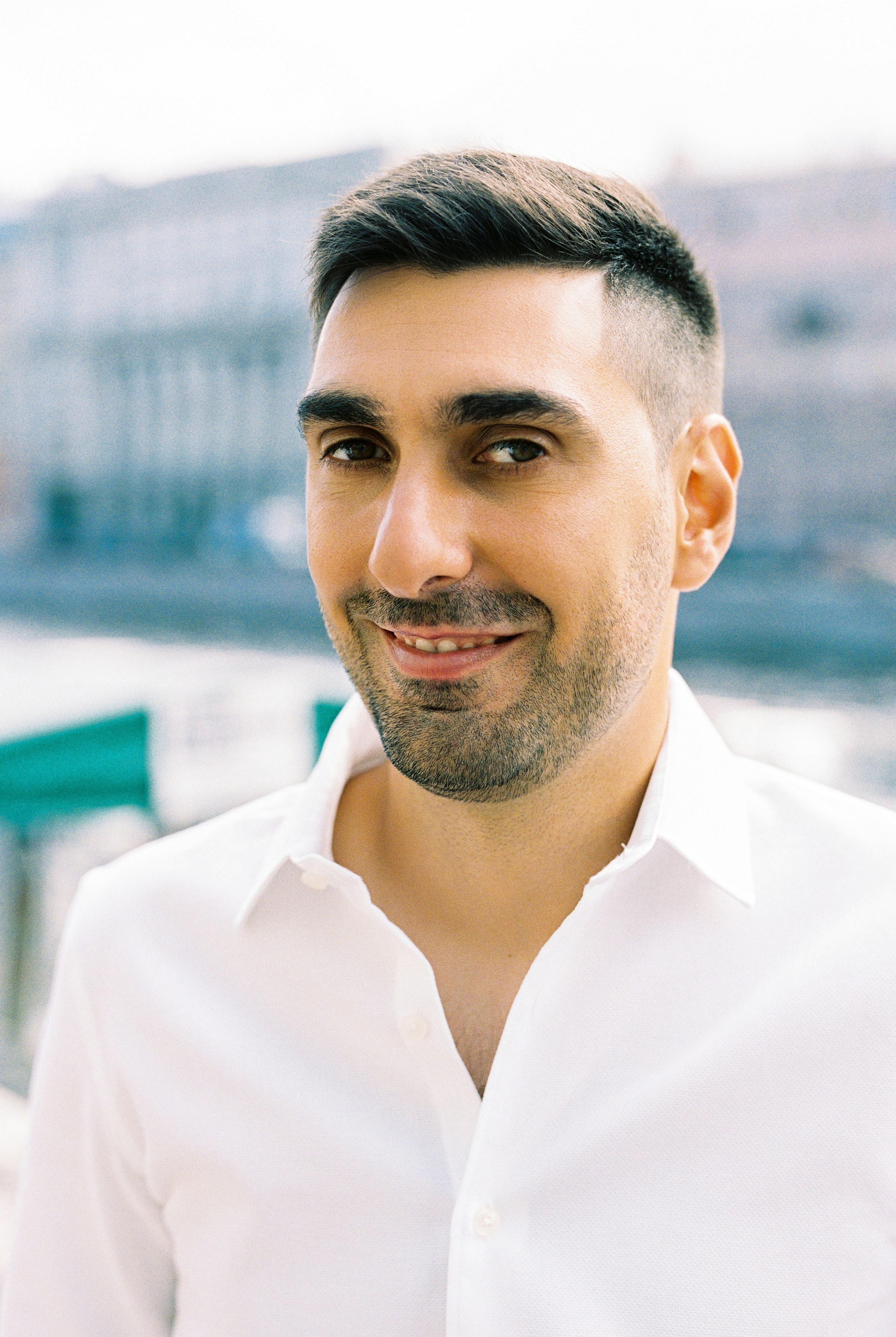 Portrait of a smiling man in a white dress shirt outdoors, showcasing confidence and warmth.