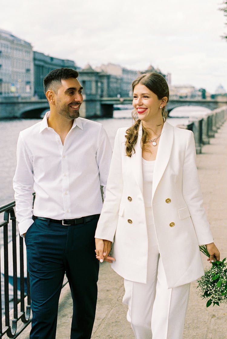 Just Married Couple Holding Hands And Walking Along City Promenade On River