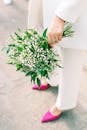 Unrecognizable Woman in White Outfit and Pink Shoes Holding Bunch of White Flowers in Hand
