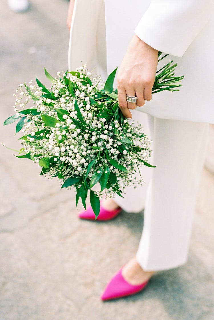 Unrecognizable Woman In White Outfit And Pink Shoes Holding Bunch Of White Flowers In Hand