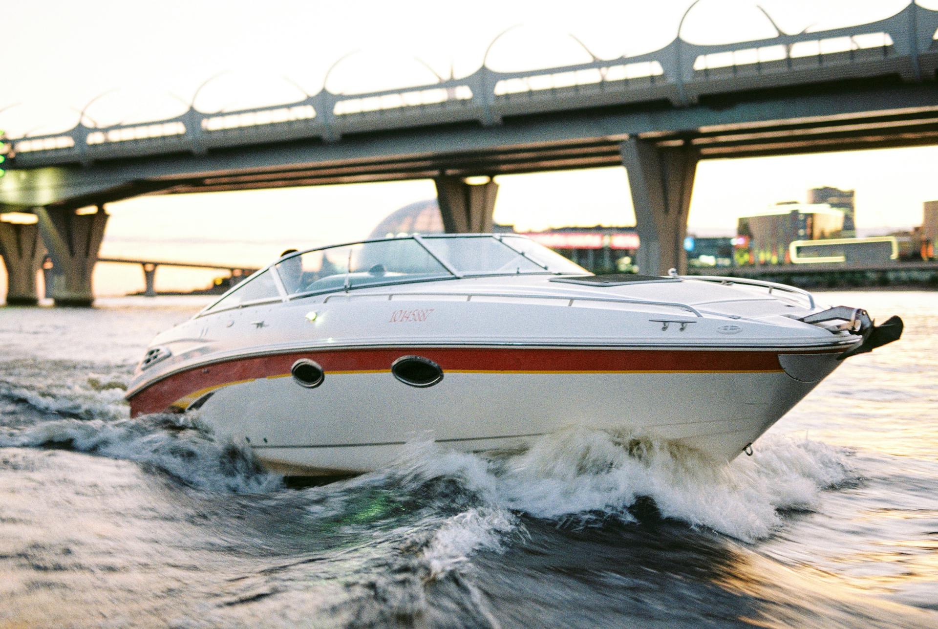A sleek motorboat speeding under a modern bridge during daylight, showcasing cityscape.