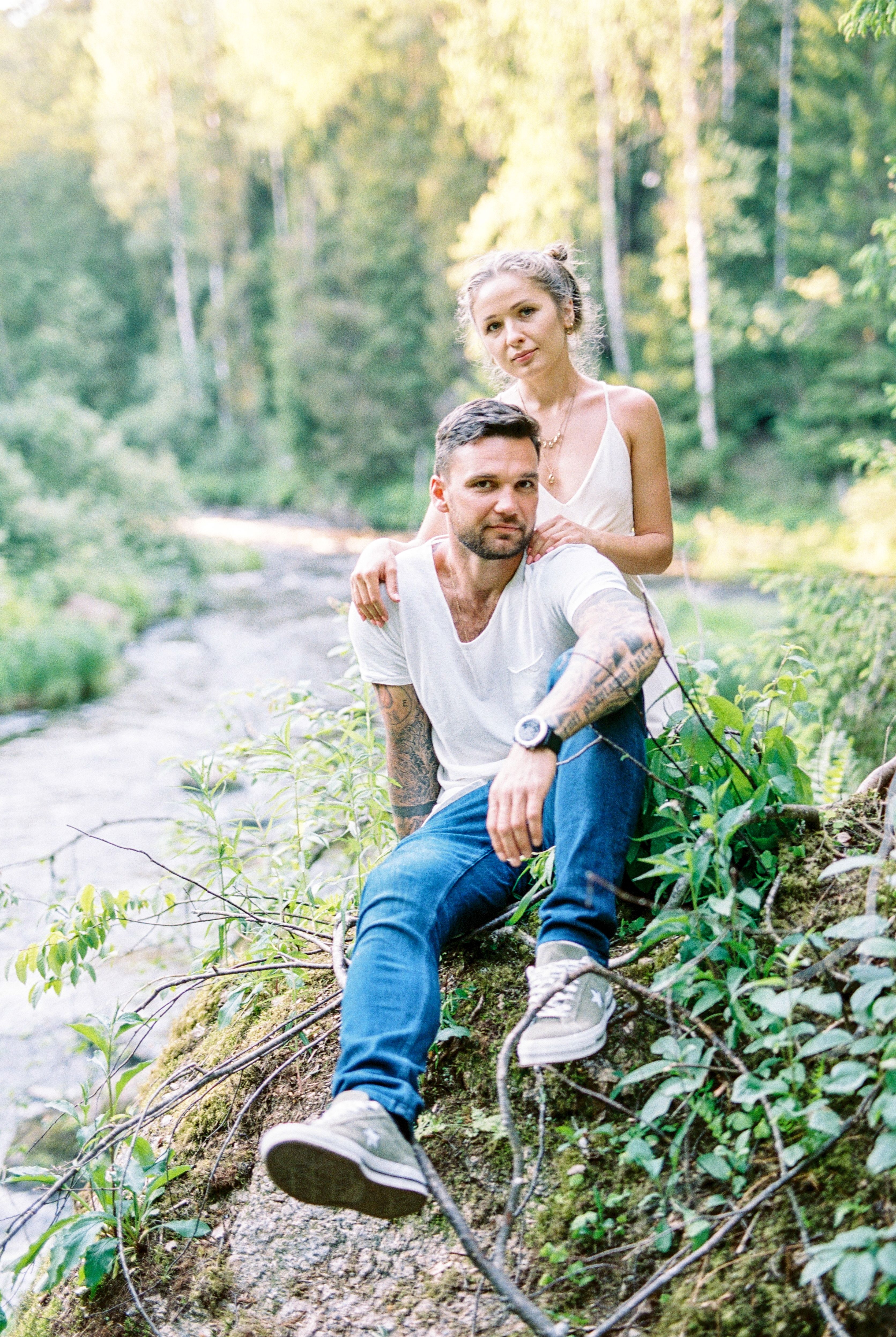 A relaxed couple enjoying a summer day by a lush forest stream, exuding harmony and nature.