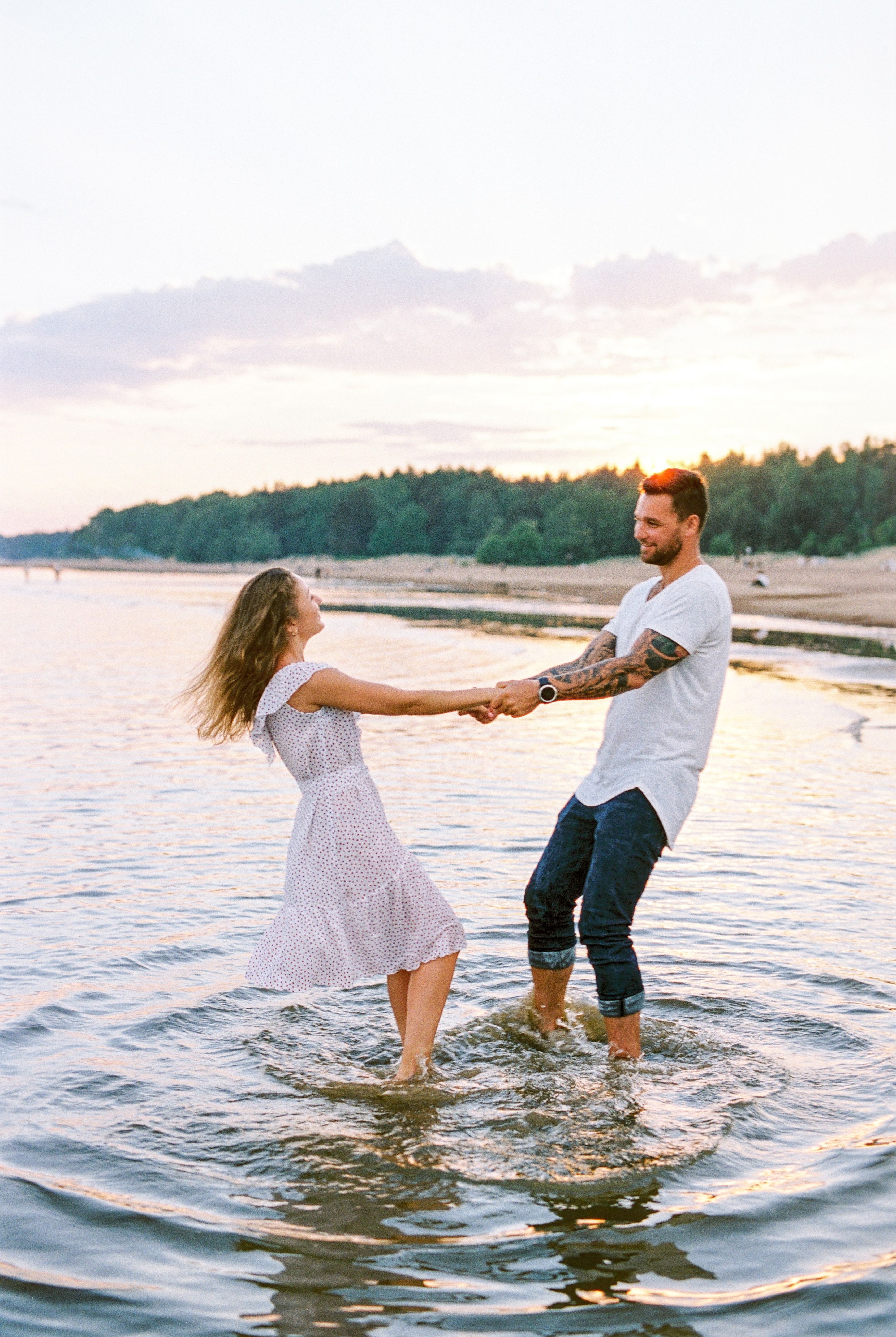 A joyful couple dances in shallow water by the lake during sunset.