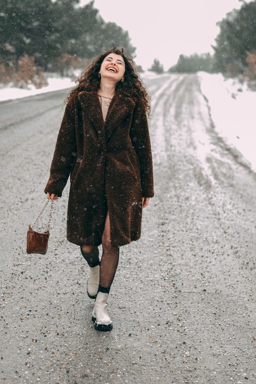 Free A happy woman enjoying a snowy walk along a winter road, capturing the essence of carefree joy and seasonal beauty. Stock Photo