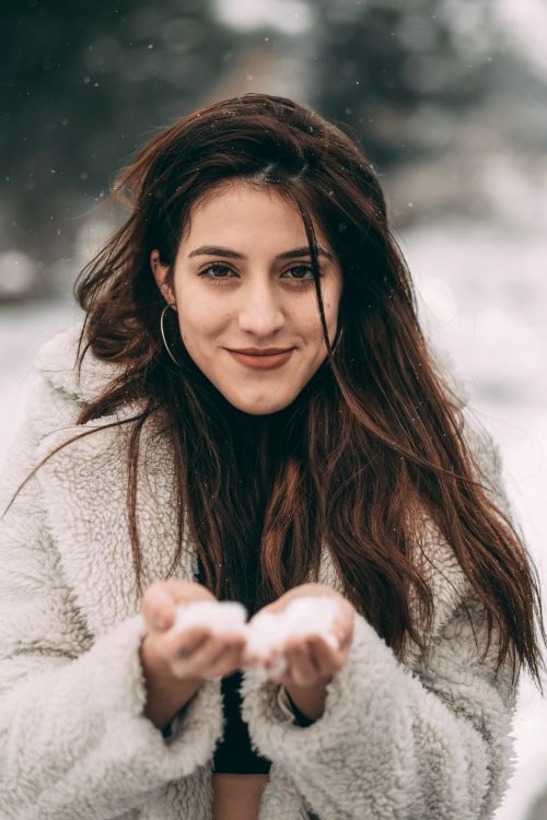 Free Smiling woman in fur coat holding snow outdoors in a winter setting. Stock Photo
