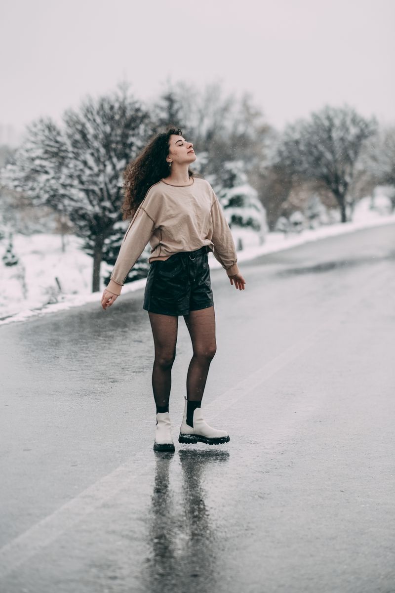 Woman in cozy sweater and white boots on snowy road