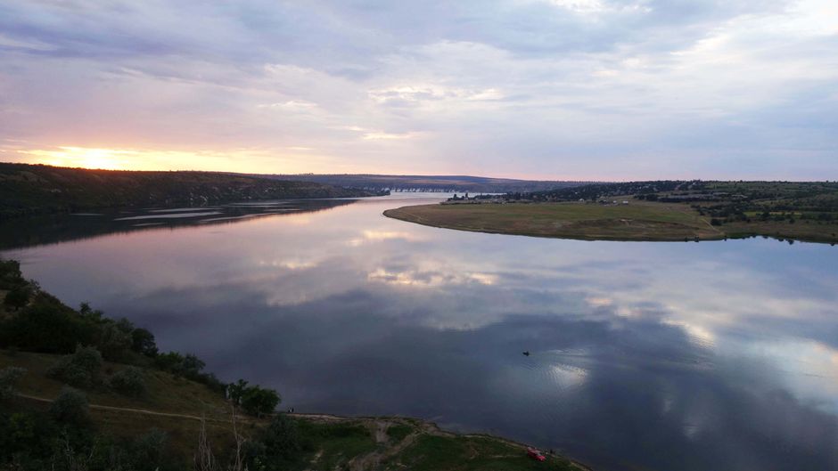 Beautiful sunset reflecting on the Dniester River near Roghi, Moldova, with calm waters and lush surroundings.