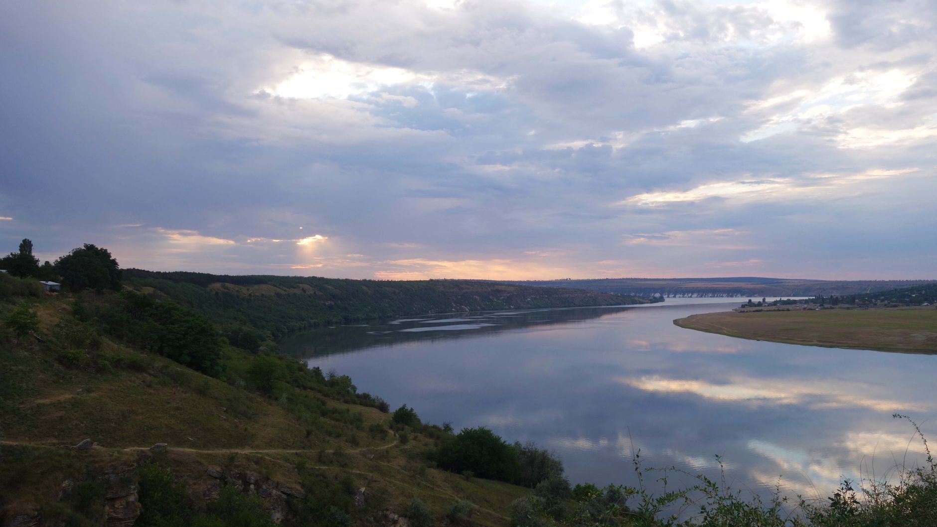 Scenic view of a river surrounded by hills under a cloudy sunset sky in Moldova.