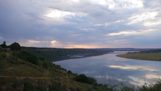 Scenic view of a river surrounded by hills under a cloudy sunset sky in Moldova.