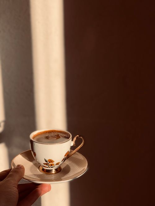 Free A vintage floral coffee cup held in warm sunlight, creating a cozy morning mood. Stock Photo