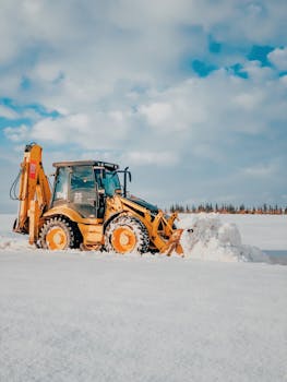 A bulldozer efficiently clears heavy snow under a bright blue sky, showcasing winter work.