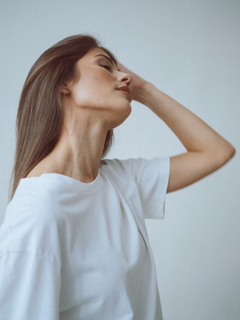 An elegant portrait of a woman with long brown hair in a white t-shirt captured in a minimalist style.
