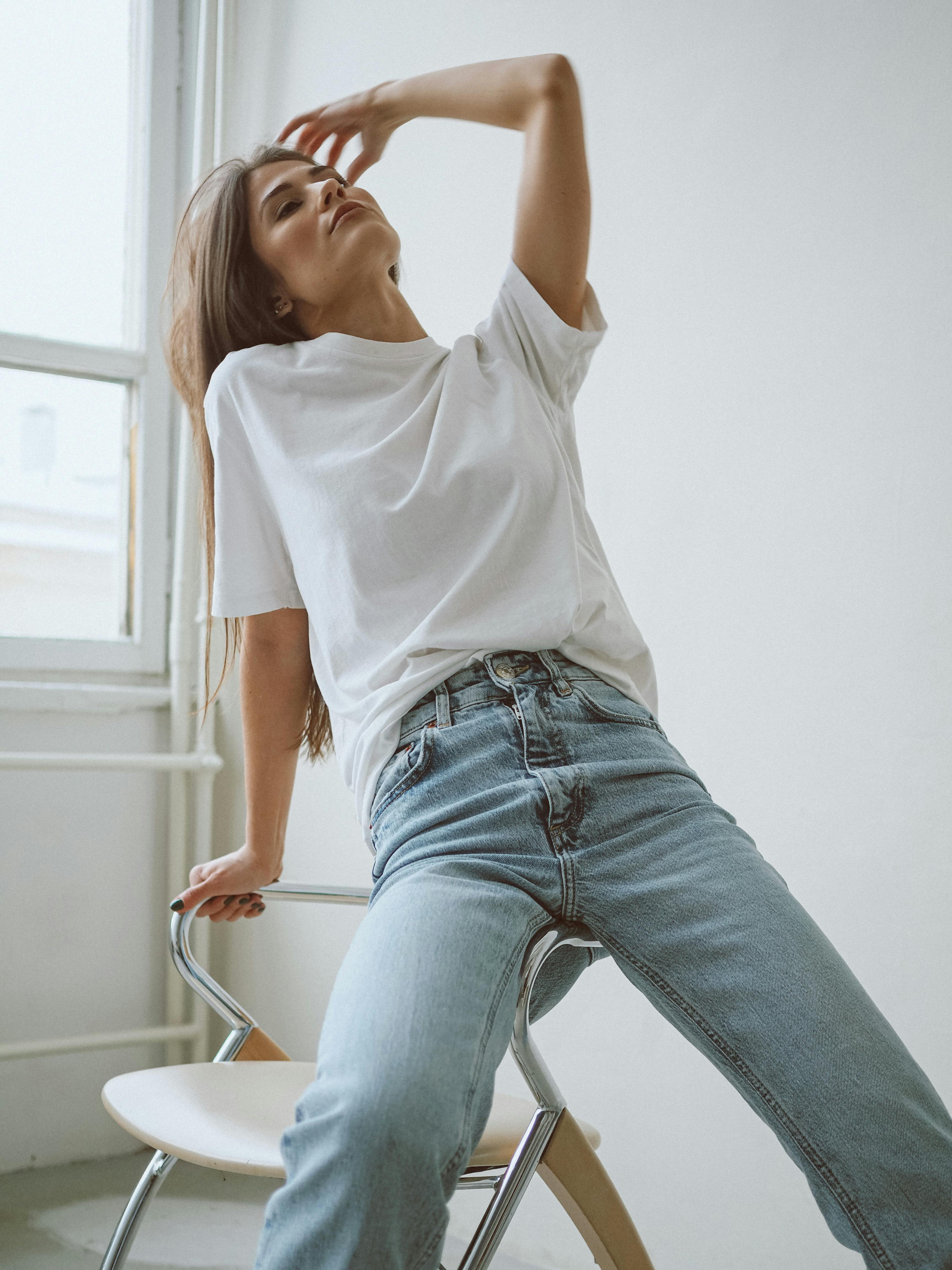 A woman in a white shirt and jeans posing elegantly in a bright room