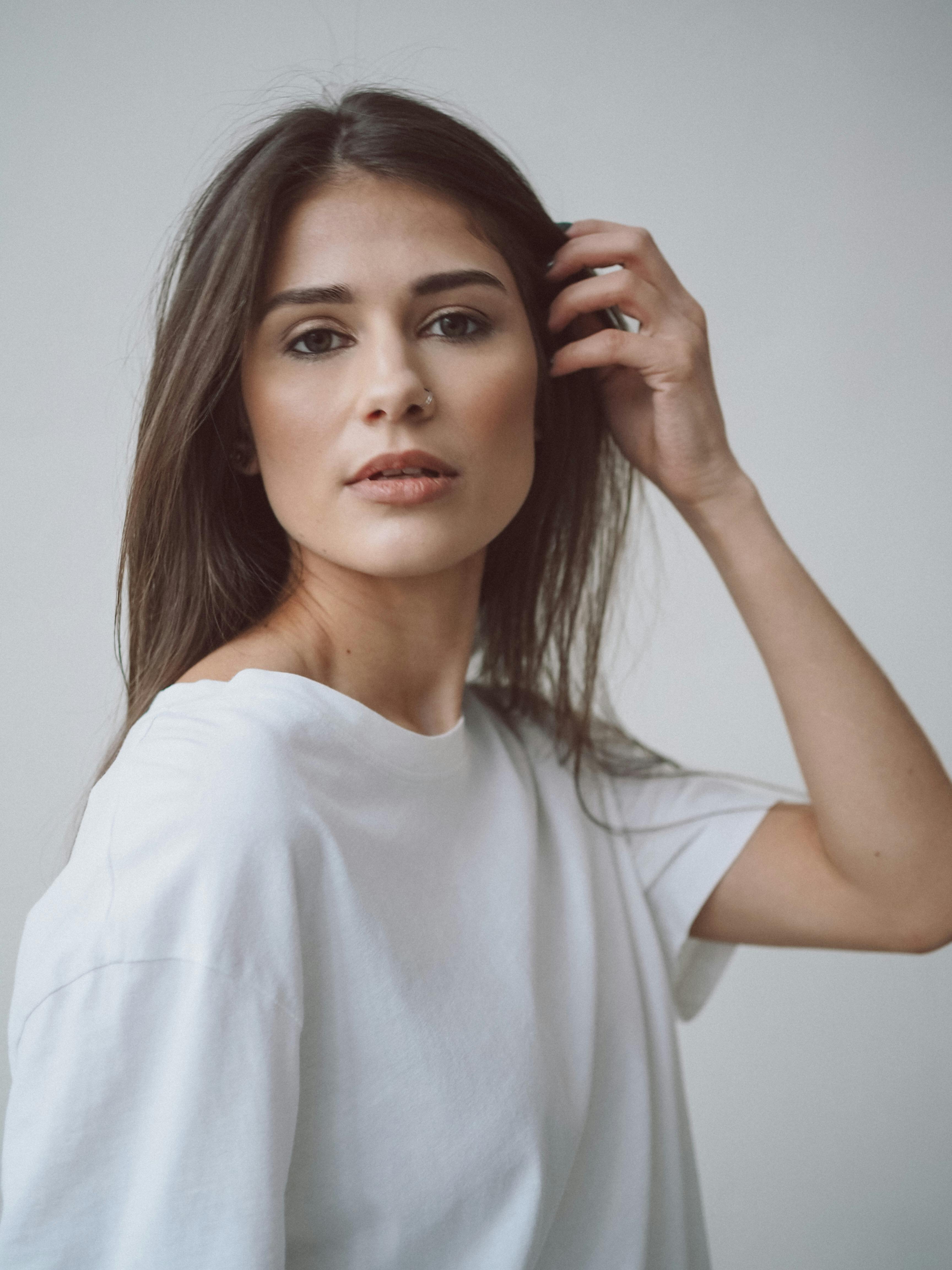 Portrait of a woman with long brown hair in a white t-shirt against a plain background.