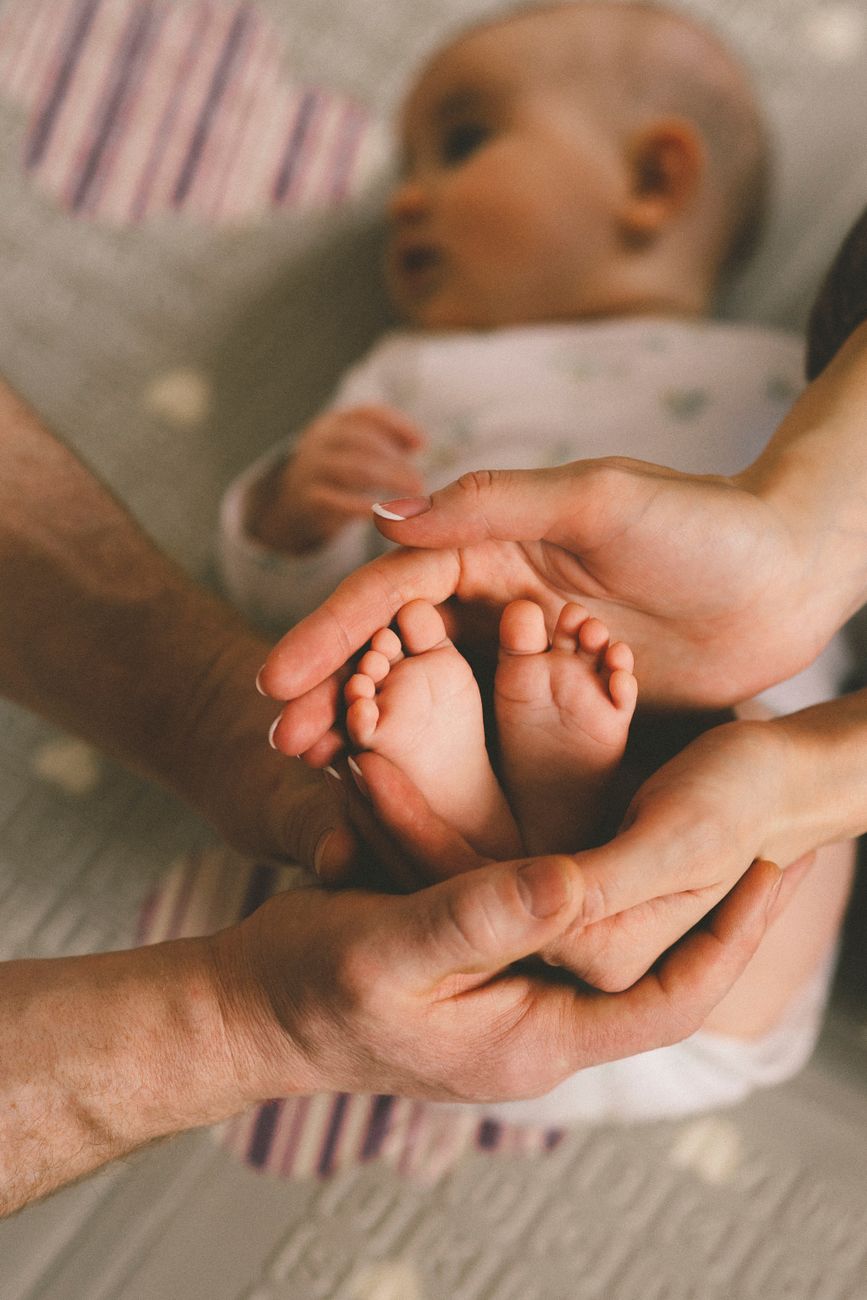 Uma família amorosa segura os pés de um bebê, simbolizando cuidado e afeto.