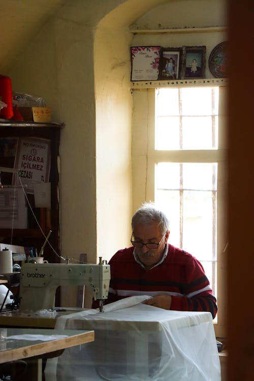 An Elderly Man Using a Sewing Machine while Holding a White Fabric