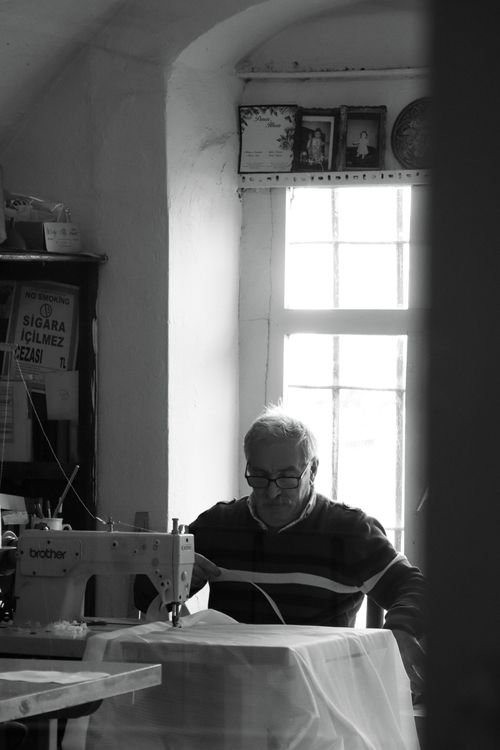 Free Monochrome image of an elderly tailor working at a sewing machine in a sunlit room. Stock Photo