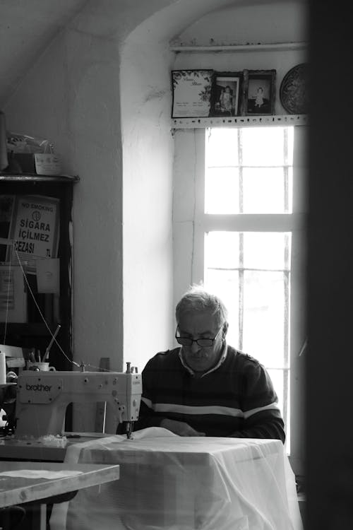 A Grayscale Photo of an Elderly Man Looking at the Sewing Machine