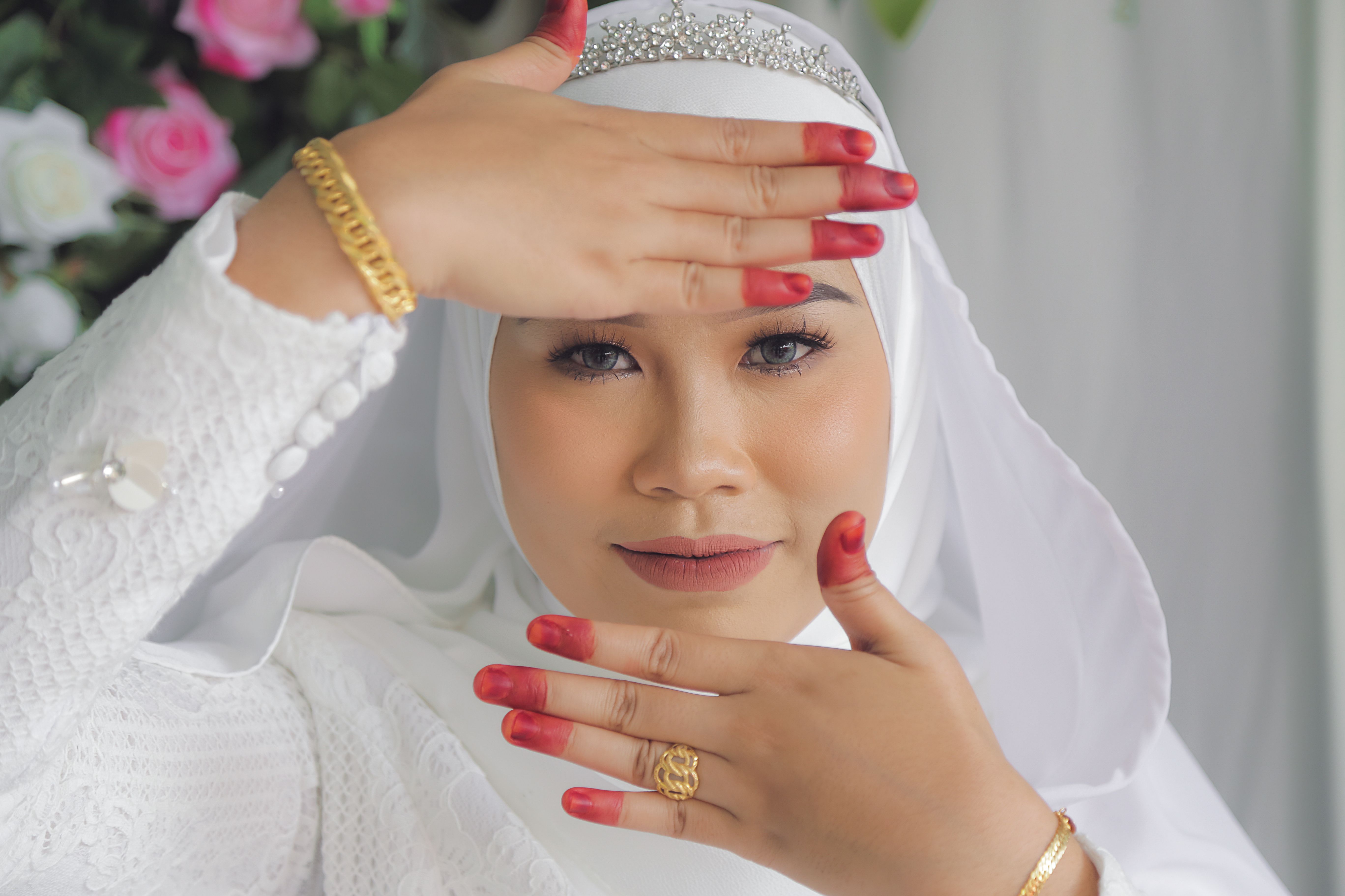 A beautiful Muslim bride in hijab showing henna-dyed hands, adorned with gold jewelry.