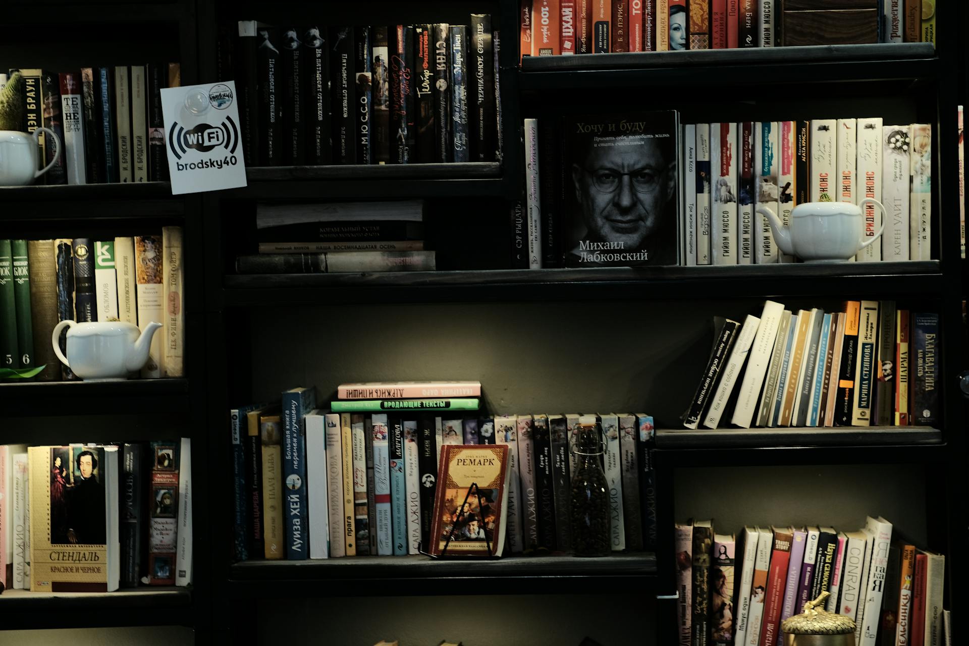 A cozy bookshelf featuring a diverse collection of books, teapots, and signage.