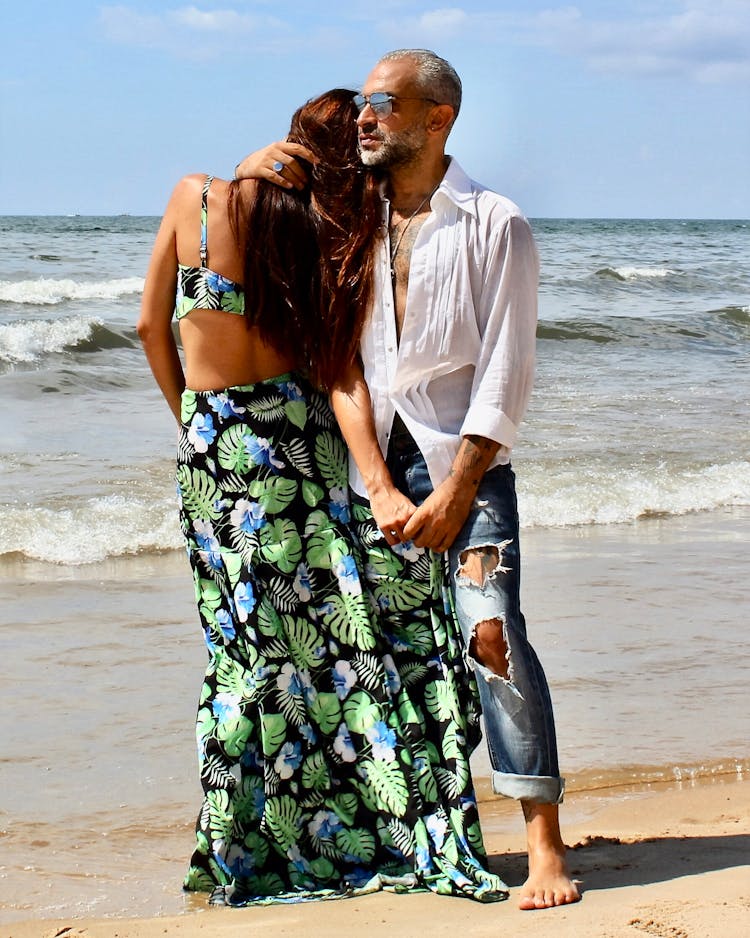 A Man And Woman Standing On The Beach Sand While Embracing Each Other