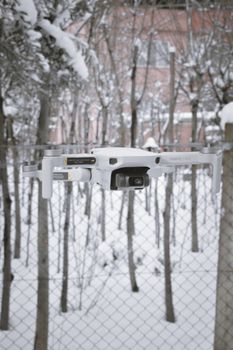 A drone captured in flight amidst snow-covered trees and a fence.