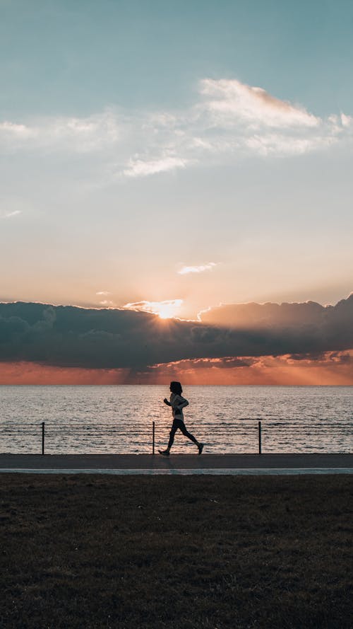 Free Silhouette of a Person Running Near a Body of Water During Sunset Stock Photo