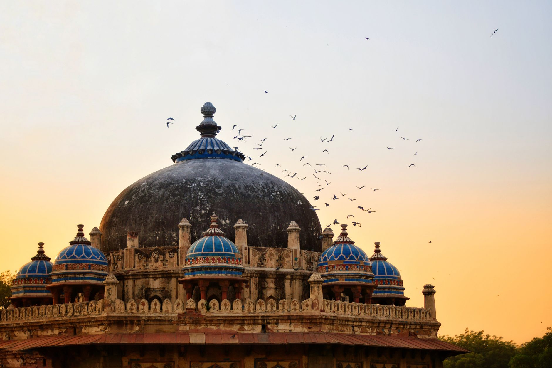 Birds flying over the historical Tomb of Isa Khan at sunrise in India.