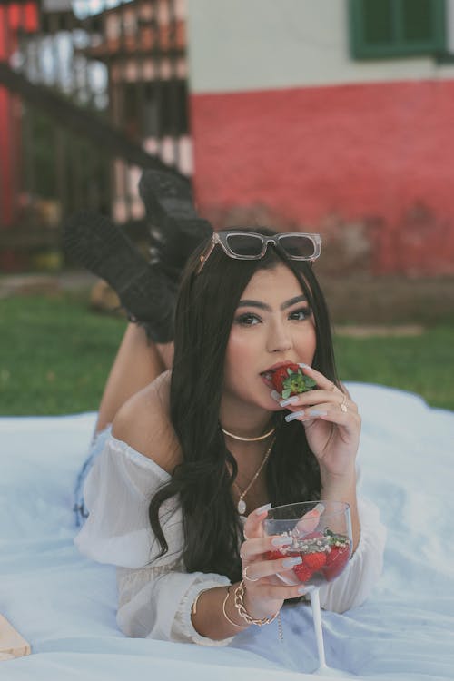 A Woman Lying on a Picnic Blanket while Eating Strawberry