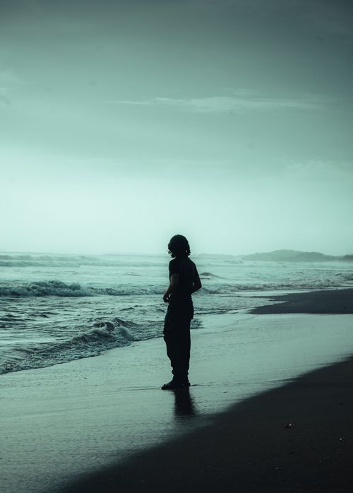 Free Silhouette of a man standing on a tranquil Indian beach at twilight, with gentle waves lapping the shore. Stock Photo