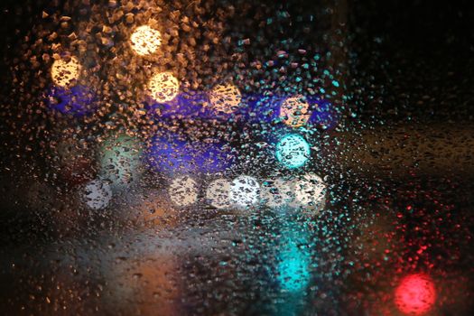 Artistic view of raindrops on a window creating a bokeh effect with city lights at night.