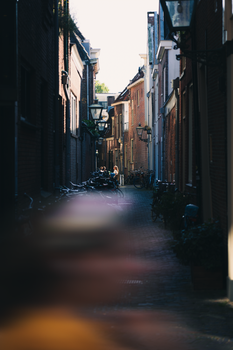 Sunlit narrow alleyway with bicycles in a classic Dutch city. Features historic architecture and ambient lighting.