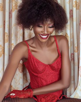 Beautiful portrait of a smiling woman with afro hair wearing red lingerie against a floral background.