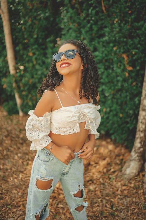 Free A Curly-Haired Woman in White Crop Top and Denim Jeans Stock Photo