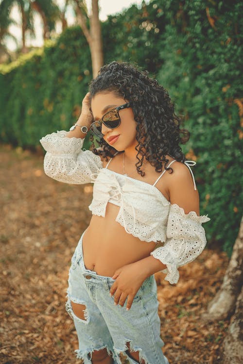 Free A Curly-Haired Woman in White Crop Top and Denim Jeans Posing Stock Photo