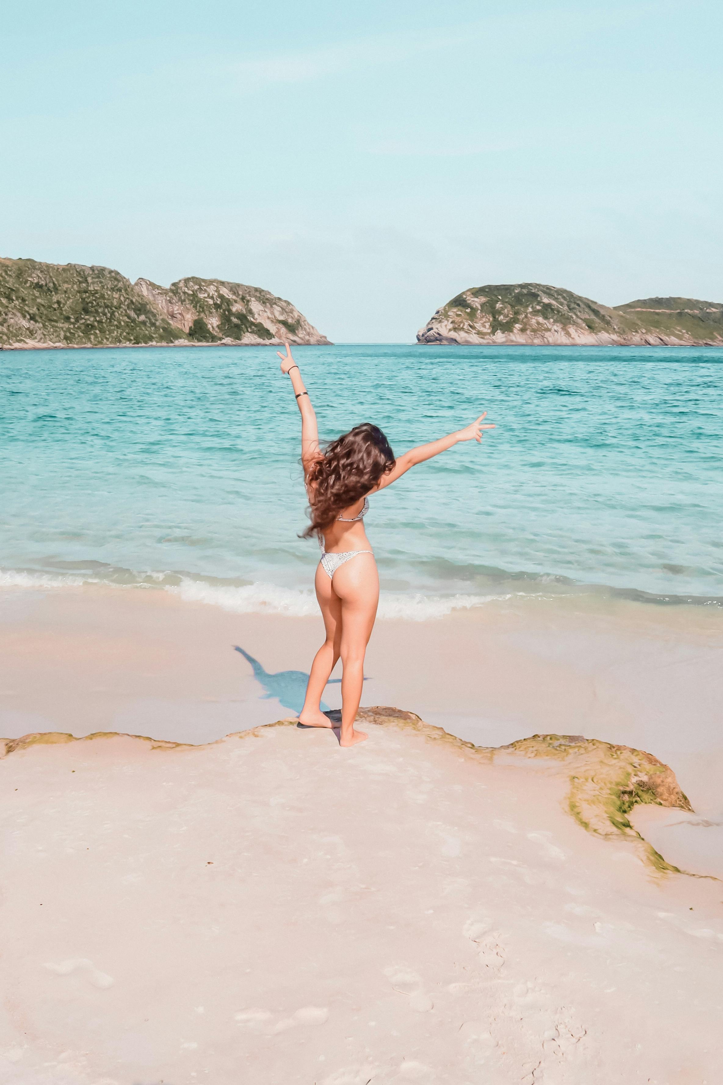 一位无忧无虑的女人在风景如画的海滩上享受阳光明媚的一天，高兴地举起双臂