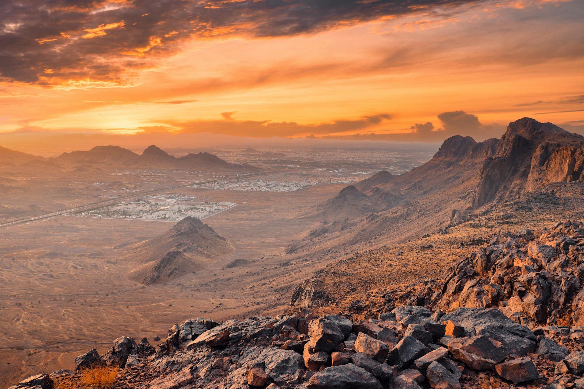 Panoramic view of rocky desert landscape in Medina, Saudi Arabia at sunset, showcasing vibrant sky and mountains.