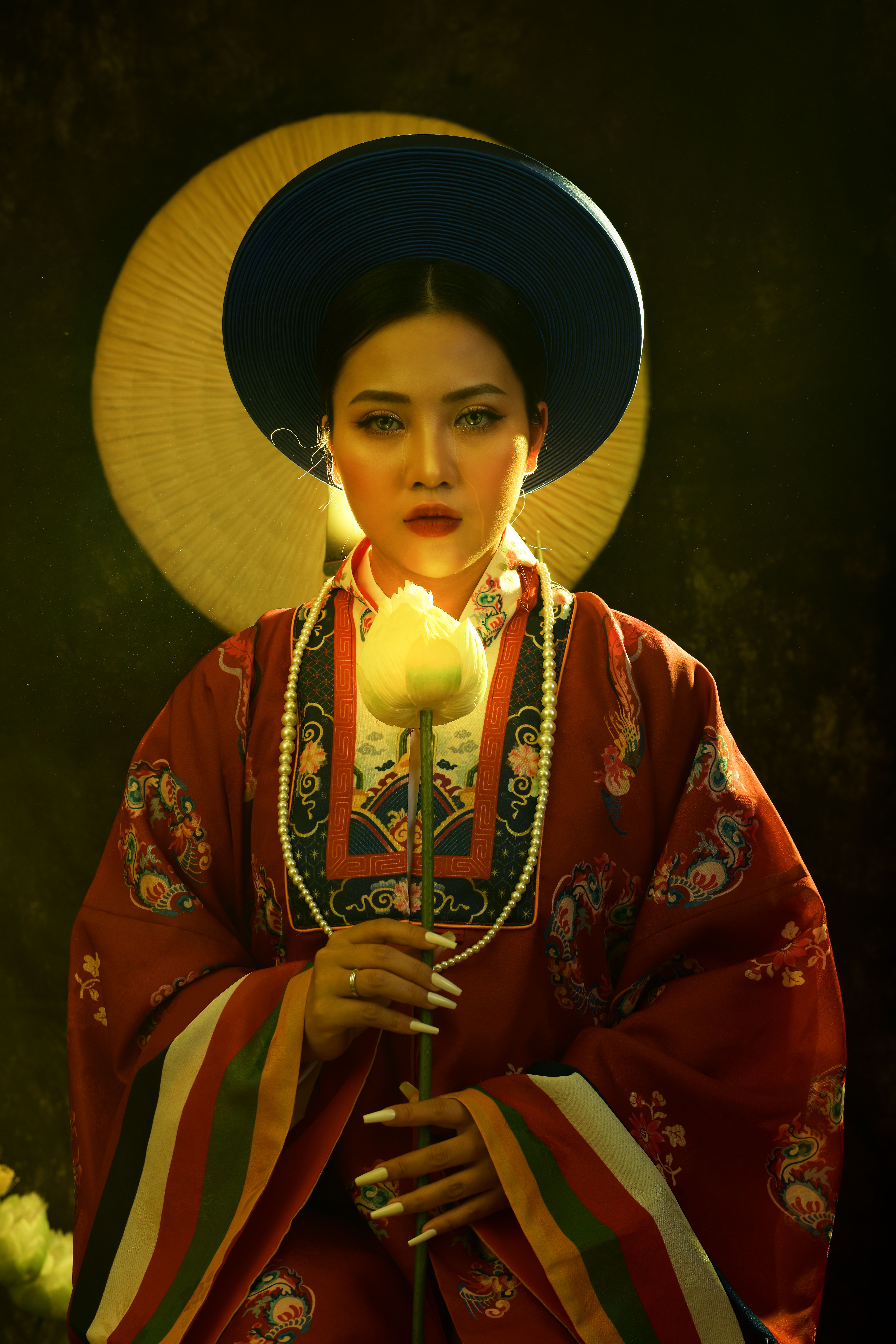 A striking portrait of a woman in traditional Asian attire holding a lotus flower, illuminated by warm light.