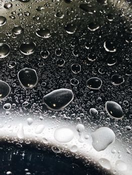 Detailed close-up of water droplets on a reflective glass surface with a moody tone.