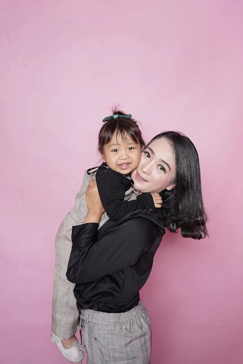 Free Woman Holding Toddler Girl Against Pink Wall Stock Photo