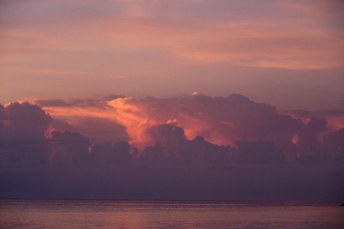 Free Stunning golden hour seascape with pink clouds reflecting on calm ocean waters at sunset. Stock Photo