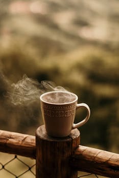 Close-up of a steaming coffee mug on a wooden railing outdoors, perfect for cozy morning themes.