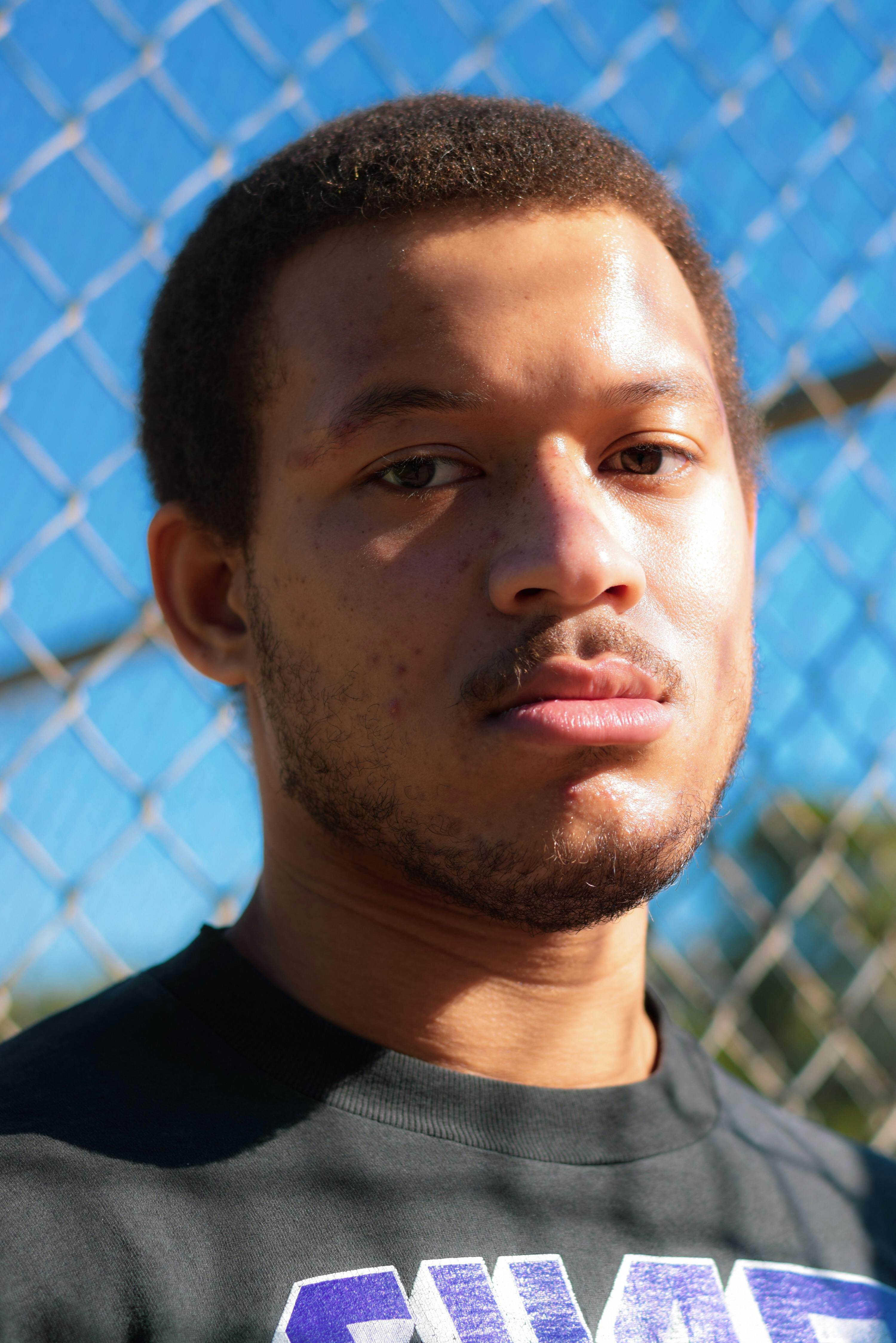 Close-up portrait of a confident young man standing outdoors against a fence.