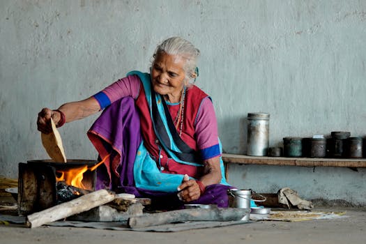 Elderly woman cooking traditional flatbread over a wood fire in India.